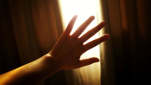 Cropped hand of woman against curtain at home