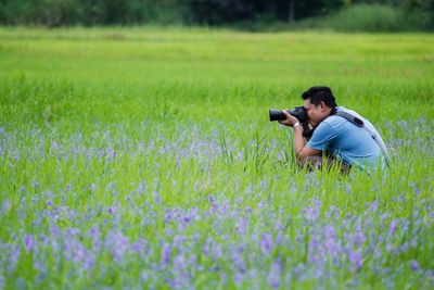 Side view of man photographing through camera while crouching on field
