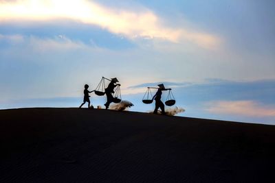 People on sand dune against sky during sunset