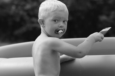 Side view portrait of cute shirtless boy sulking pacifier while playing in lawn