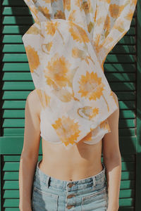 Woman covering face with curtain while standing against wall