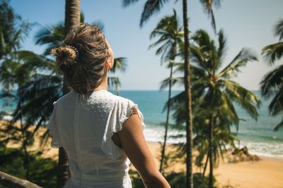 Rear view of woman standing by palm tree at beach