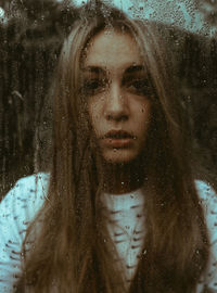 Close-up portrait of woman with wet glass window in rain