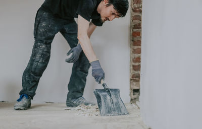 A young man collects construction waste with a dustpan. person