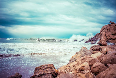 Person surfing on wave in sea against cloudy sky