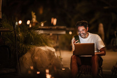 Happy man using phone and laptop at night