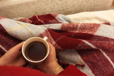 Close-up of hand holding coffee cup on bed