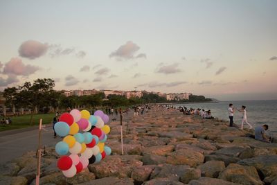 Group of people on rocks at beach against sky during sunset