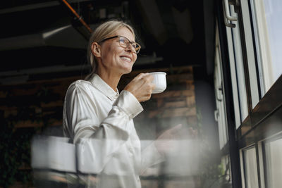 Smiling businesswomanholding cup of coffee looking out of window
