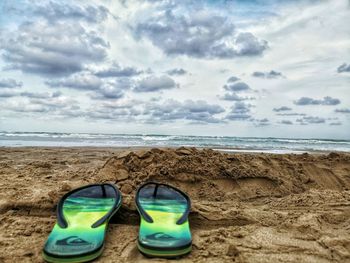 Close-up of shoes on sand at beach against sky