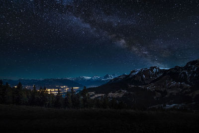 Scenic view of landscape and mountains against star field at night