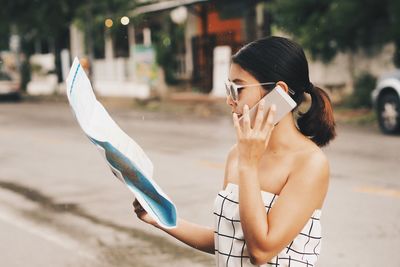 Mid adult woman with world map using phone on street