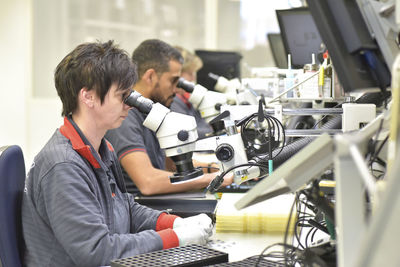 Woman using a microscope for the quality control in the manufacturing of circuit boards for the electronics industry