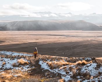 Rear view of woman walking on landscape against sky during winter