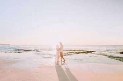 Rear view of couple standing at beach against sky