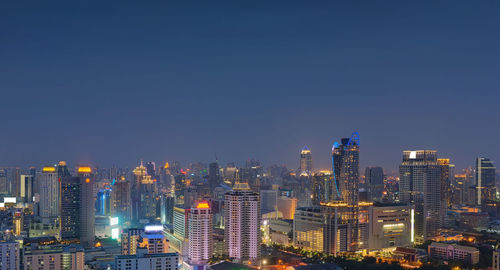 Illuminated cityscape against clear blue sky at night