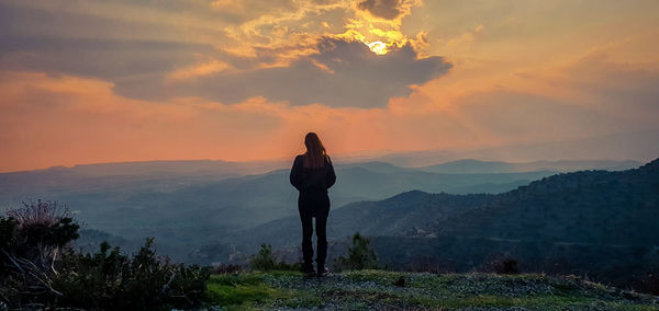 Rear view of woman standing on mountain during sunset