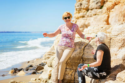 Two elderly women are happy to meet each other, sitting on rock on the seashore