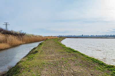 Footpath by canal against sky