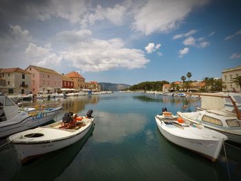 Boats moored in harbor by buildings against sky