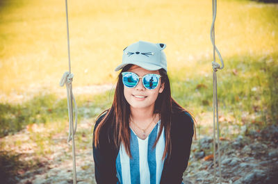 Portrait of smiling young woman sitting on swing on land