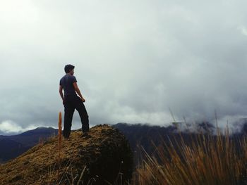 Rear view full length of man standing on rock against cloudy sky