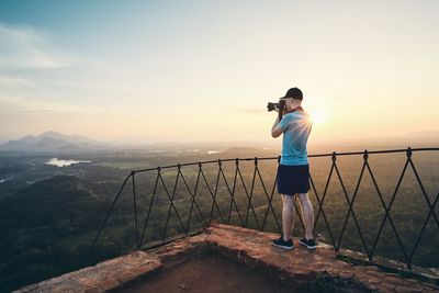 Man photographing landscape against sky during sunset