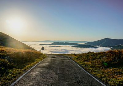 Road leading towards mountains against clear sky