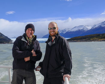 Portrait of smiling friends standing on boat at sea against mountain