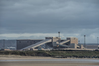 View of factory by sea against sky