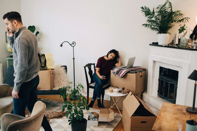 Man talking on mobile phone and woman using laptop at new home