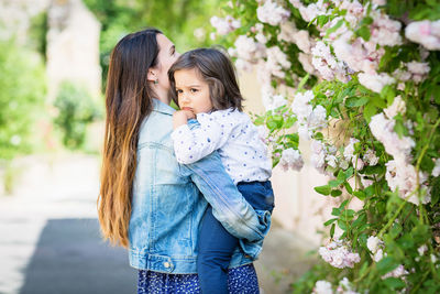 Mother and little handsome baby boy looking at bush with white roses