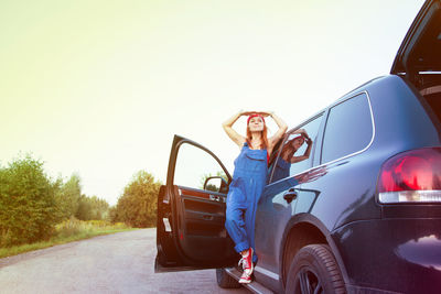 Mechanic standing on breakdown car against sky