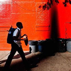 Side view of man walking against red wall