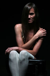 Young woman sitting against black background