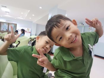 Portrait of happy male friends gesturing peace sign in classroom