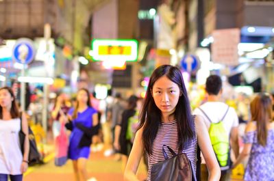 Portrait of young woman standing on illuminated street at night