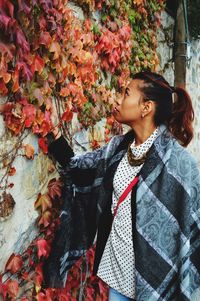 Young woman looking away while standing by leaves on wall during autumn