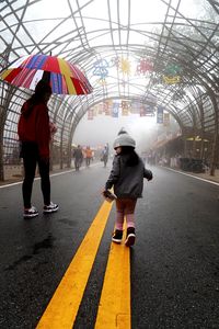 Rear view of girl with mother walking on road in city during foggy weather