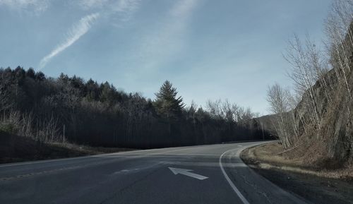 Empty road by trees against sky