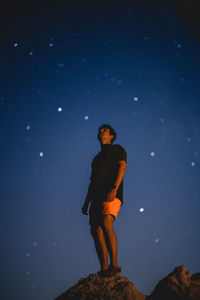 Low angle view of young man standing on rock under stars