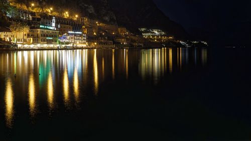 Illuminated buildings by lake against sky in city at night