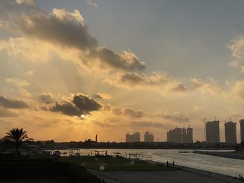 City buildings by sea against sky during sunset