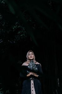 Portrait of a young woman standing against trees at night