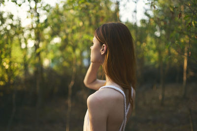 Side view of a young woman against trees