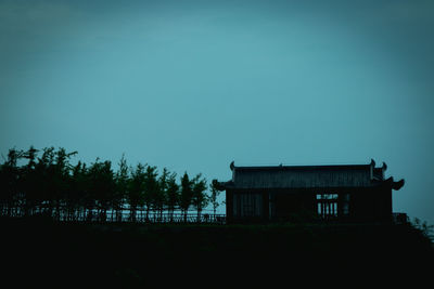 Low angle view of silhouette trees and building against sky