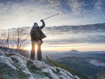 Woman reached mount peak. girl wearing backpack and using trekking sticks, enjoying daybreak