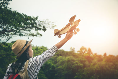 Teenage girl with toy plane in forest against sky