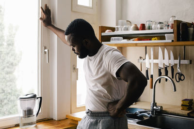 Depressed lonely man with hand on hip standing in kitchen at home