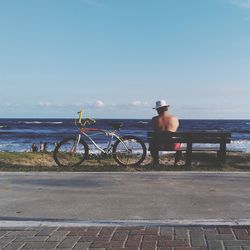 Man riding bicycle on bench by sea against clear sky